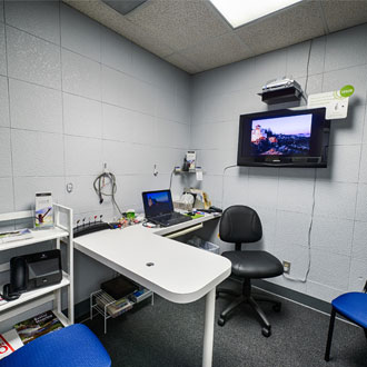 room at Bisel Hearing Aid center with tv on wall and desk with chair and laptop